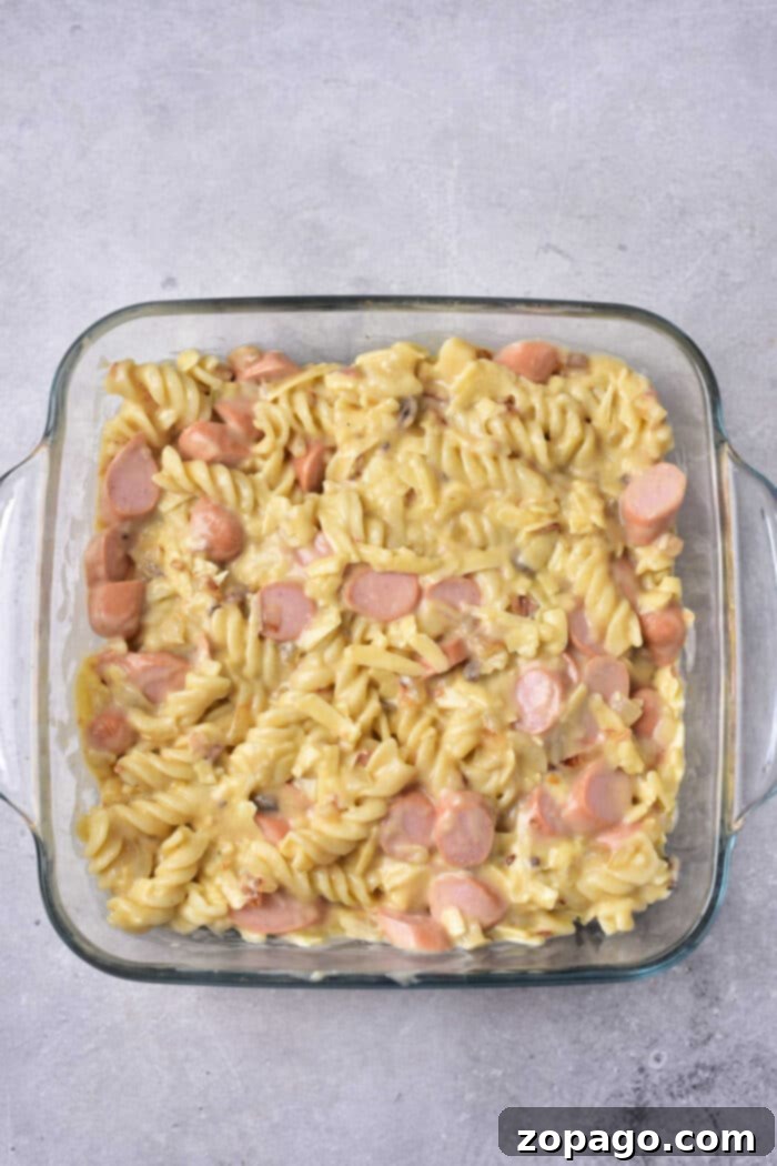 Cheesy Hot Dog Casserole Bake 5 A hearty chili cheese dog casserole, baked with a golden cheese topping, sliced hot dogs, and pasta, ready to be served from a glass dish.