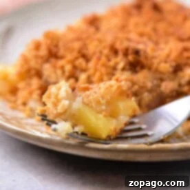 A fork holding a bite of pineapple crumble topped with crispy golden crust sits invitingly on a beige plate, reminiscent of a delightful twist on the classic pineapple casserole recipe.
