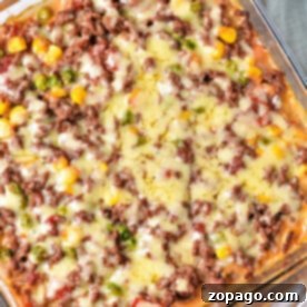 The Shipwreck Casserole is a delightful baked dish featuring ground meat, melted cheese, corn, peas, and tomatoes all layered beautifully in a square glass dish.