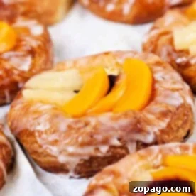 Puff Pastry Breakfast Ideas 4 Close-up of delightful puff pastry breakfast creations, glazed and topped with sliced peaches on a pristine white surface.