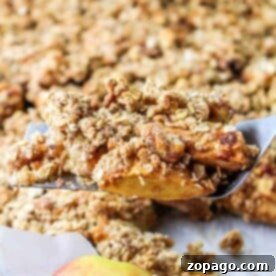 A spatula holds a freshly baked apple crumble piece, the perfect showcase for your apple slices recipe, with a whole apple in the foreground.