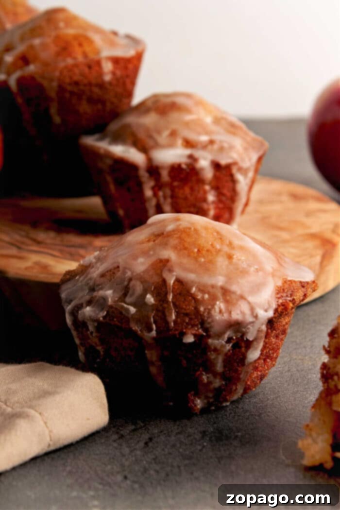 Sweet & Spiced Apple Fritter Muffins 6 A close-up of three artfully glazed apple fritter muffins resting on a wooden board, with a beautifully blurred background that emphasizes their homemade appeal and delicious finish.