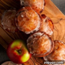 Freshly baked apple fritter muffins with glaze on a wooden board, complemented by two green and red apples, embodying the essence of baked apple fritters.