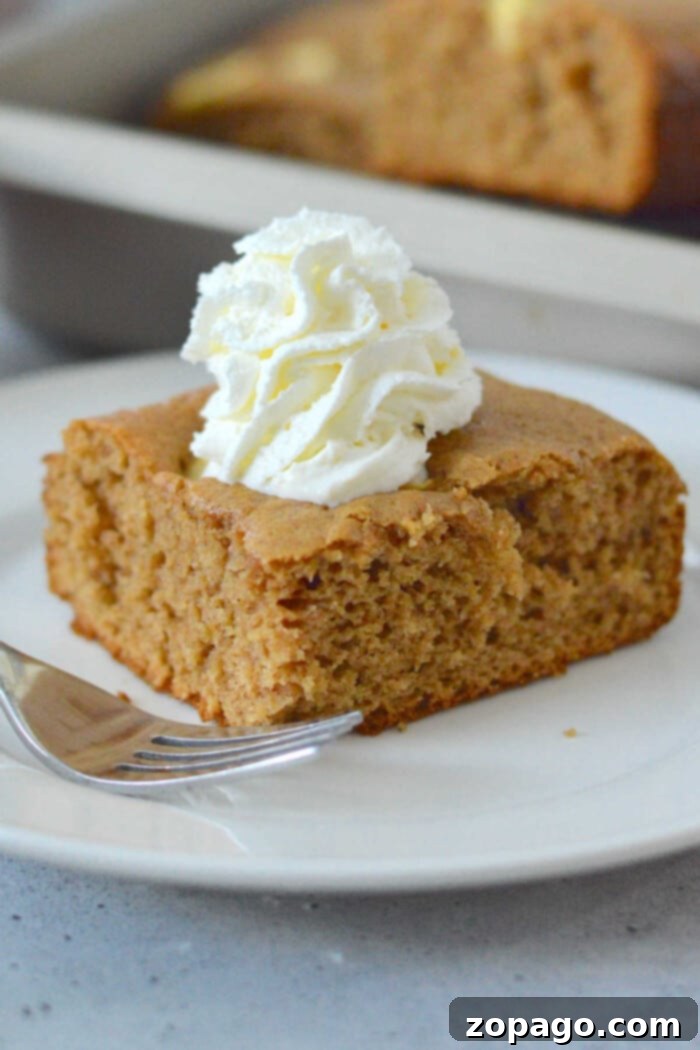 Easy Apple Cake from a Box Mix 7 A slice of brown apple cake made with cake mix is topped with whipped cream on a white plate, with a fork beside it.