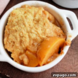 A delicious crockpot peach cobbler with cake mix, served beautifully in a small white dish on a wooden surface.