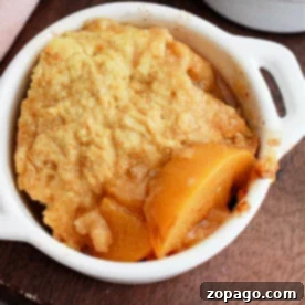 Slow Cooker Peachy Dump Cake 6 A delicious crockpot peach cobbler with cake mix, served beautifully in a small white dish on a wooden surface.