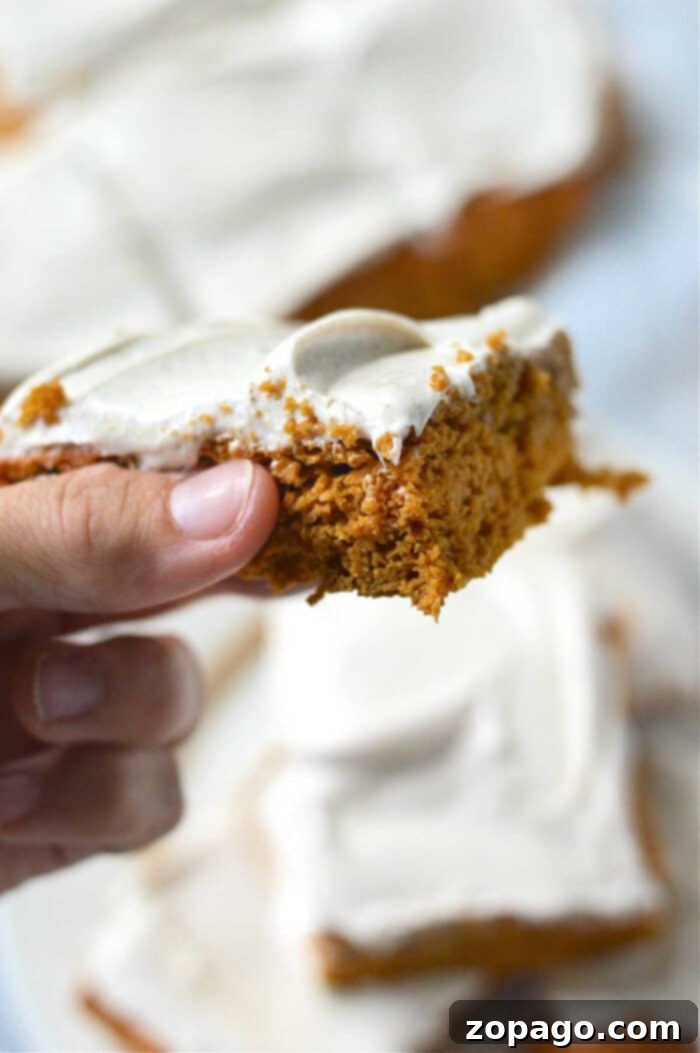 Easy Cake Mix Pumpkin Bars 2 Close-up of a hand holding pumpkin bars made with cake mix, and more cake pieces in the background.