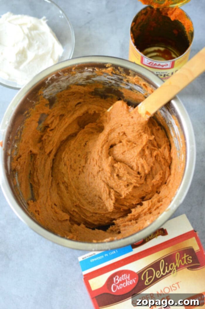 Easy Cake Mix Pumpkin Bars 4 A mixing bowl filled with pumpkin cake bars batter sits on a gray surface, surrounded by canned pumpkin and a cake mix box, ready to whip up delicious pumpkin bars with cake mix. Nearby, whipped topping waits to add the finishing touch.