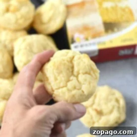 A hand holding a delectable cookie, with more cake mix cookies with cream cheese and a cake mix box in the background.