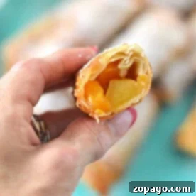 A hand holds a delightful pastry, reminiscent of peach cobbler egg rolls, with a turquoise plate in the background.