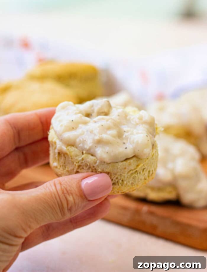 Pillowy Plant-Based Biscuits with Savory Gravy 2 Close-up of golden brown vegan biscuits served with a generous pour of creamy, white vegan gravy, garnished with fresh herbs.