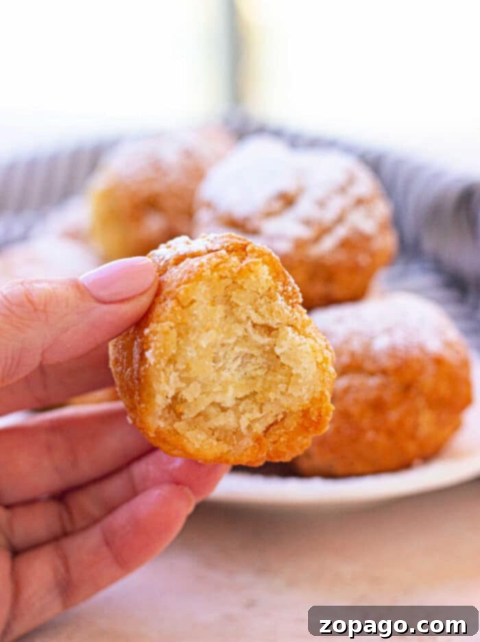 Sweet Biscuit Poppers 2 A hand delicately holds a partially eaten fried biscuit donut hole, with a plate piled high with similar treats tempting in the background.