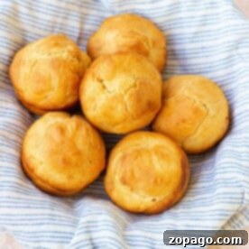 Golden brown mayonnaise biscuits rest in a striped cloth-lined basket on a light textured surface.