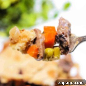 Close-up of a fork holding a bite of leftover steak pot pie with carrots, peas, and golden crust.