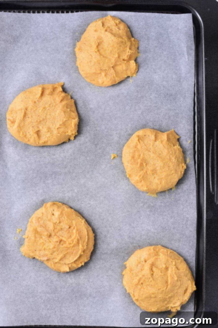 Creamy Pumpkin Cheesecake Cookies 5 Five unbaked Pumpkin Cream Cheese Cookies, rest on a parchment-lined baking tray.
