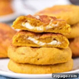 Pumpkin Cream Cheese Cookies stacked on a plate, each filled with rich cream cheese, one cookie broken to reveal its delicious filling.