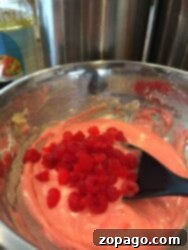 Bursting Cherry Bread 4 A bowl of pink Maraschino Cherry Bread batter with chopped red cherries being mixed with a black spatula.