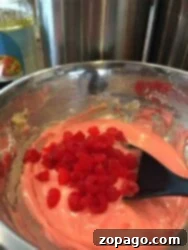 Homemade Cherry Loaf 4 A bowl of pink Maraschino Cherry Bread batter with chopped red cherries being mixed with a black spatula.
