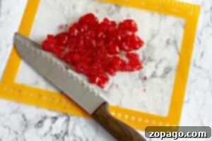 Homemade Cherry Loaf 5 Chopped red candied cherries, perfect for Maraschino Cherry Bread, are spread on a cutting mat with a knife on a marble countertop.