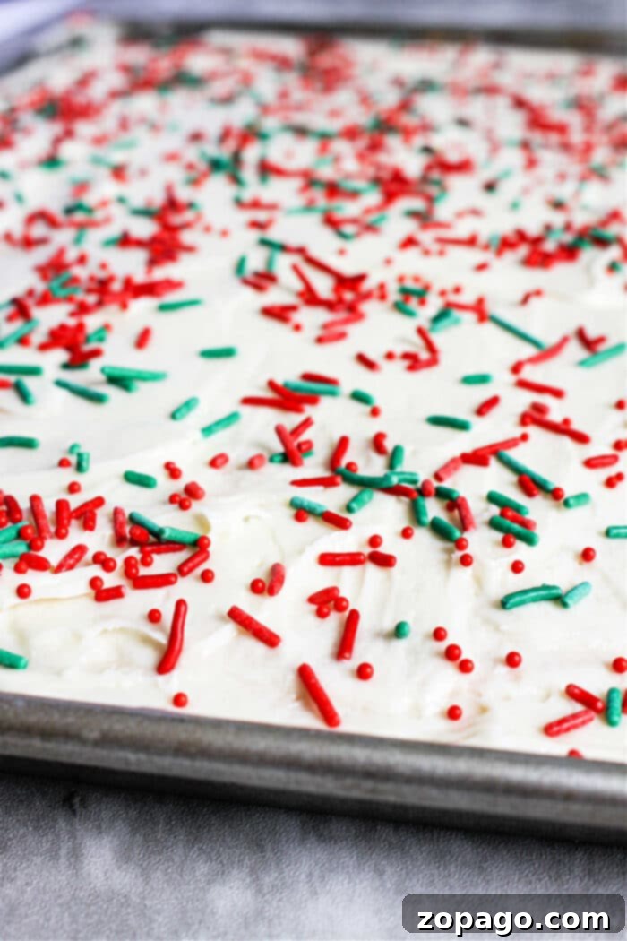Easy Sugar Cookie Bars 5 Festive cookie bars covered with white frosting and adorned with red and green sprinkles sits invitingly in a baking tray, reminiscent of delightful Christmas bar cookies.
