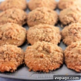 A muffin tray filled with crumb-topped peach cobbler muffins on a light background.