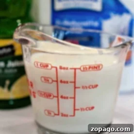 A measuring cup filled with milk, the first step in how to make buttermilk with lemon juice, stands surrounded by zesty lemon juice and milk carton containers.