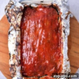 Glazed venison meatloaf recipe nestled in a foil-lined loaf pan on a wooden board.