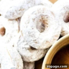Perfect Powdered Sugar Donuts 8 A close-up of several powdered sugar donuts stacked on a plate, with a cup filled with a rich, brown liquid, likely coffee or tea.