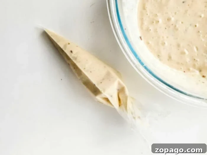 How to Make Funnel Cake Batter: A close-up shot of funnel cake batter being poured into a freezer bag, demonstrating a simple technique for creating the iconic swirl.
