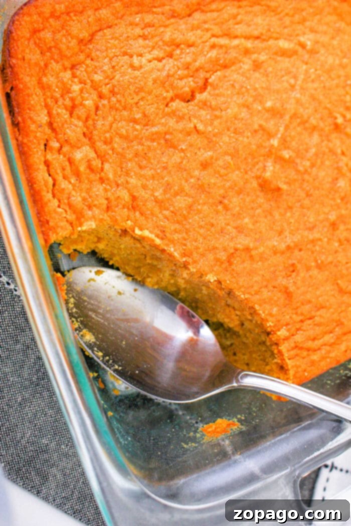 Melt-in-Your-Mouth Spoonbread 2 A glass dish showcases a baked spoonbread, partially scooped with a spoon—a delightful sweet potato spoonbread recipe waiting to be shared.