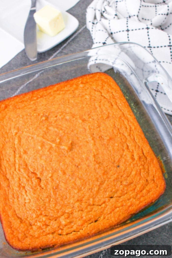 Southern Spoonbread Delight 6 Golden-brown sweet potato corn pudding made from a classic spoonbread recipe sits in a glass dish, accompanied by a plate with butter and a checkered towel.