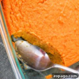 A glass dish showcases a baked spoonbread, partially scooped with a spoon—a delightful sweet potato spoonbread recipe waiting to be shared.