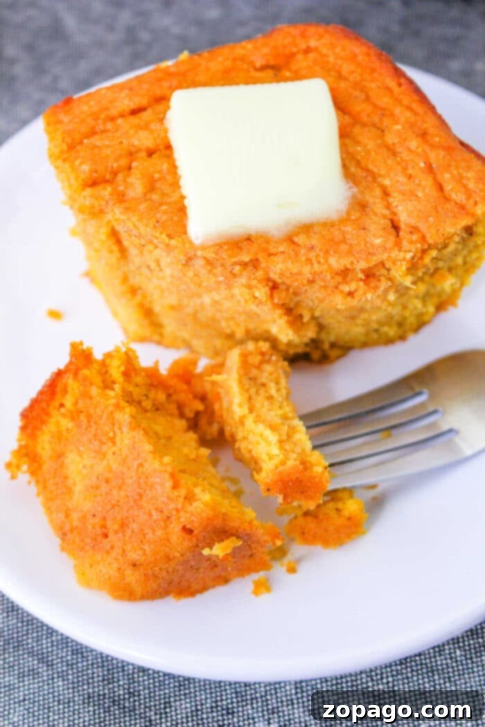 Southern Spoonbread Delight 8 A slice of delicious spoonbread recipe, sits on a white plate with a pat of butter melting on top and a fork beside it.