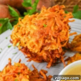 Sweet potato latkes on a plate with a side of applesauce, garnished with herbs.