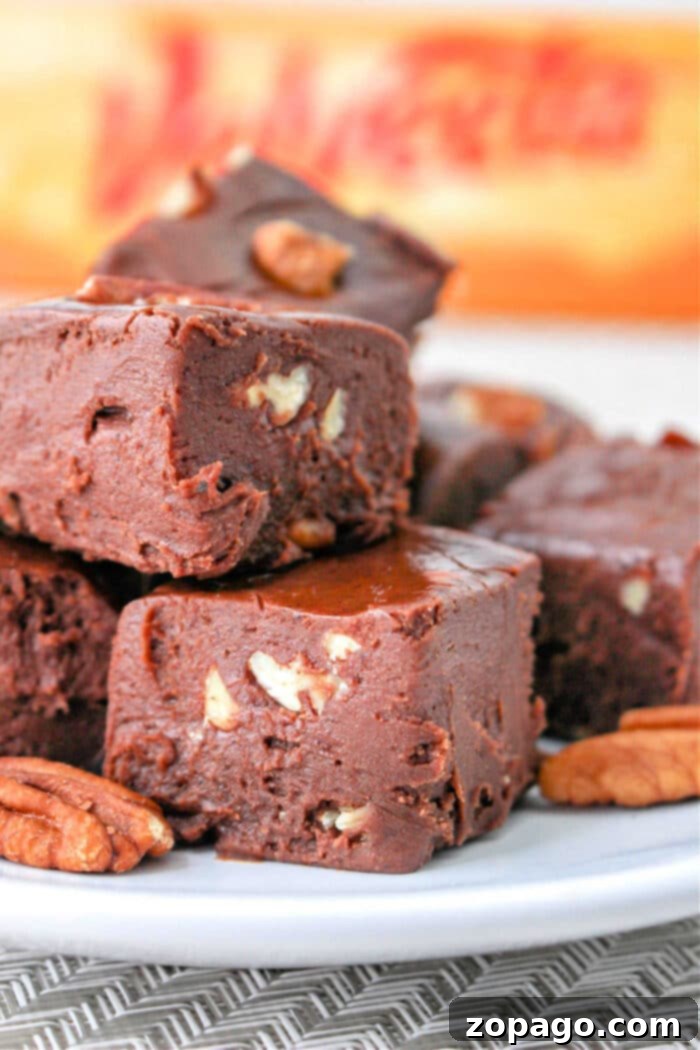 Creamy Velveeta Fudge 2 Close-up of decadent chocolate fudge with Velveeta and pecan pieces stacked on a plate, showcasing its smooth texture.