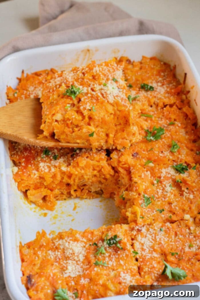 Homestyle Carrot Casserole 6 Cheesy carrot casserole in a white baking dish, topped with parsley, with a wooden spatula serving a piece.
