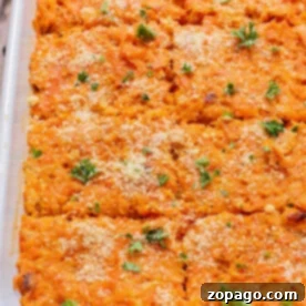 Baked sweet potato and carrot casserole in a dish, topped with breadcrumbs and fresh herbs, cut into square portions.