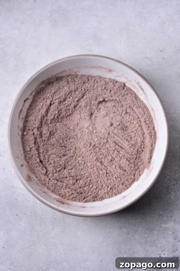Molten Chocolate Brownie Loaf 3 A bowl of mixed cocoa powder, perfect for whipping up a delightful brownie bread, sits gracefully in a white bowl on a textured gray surface.