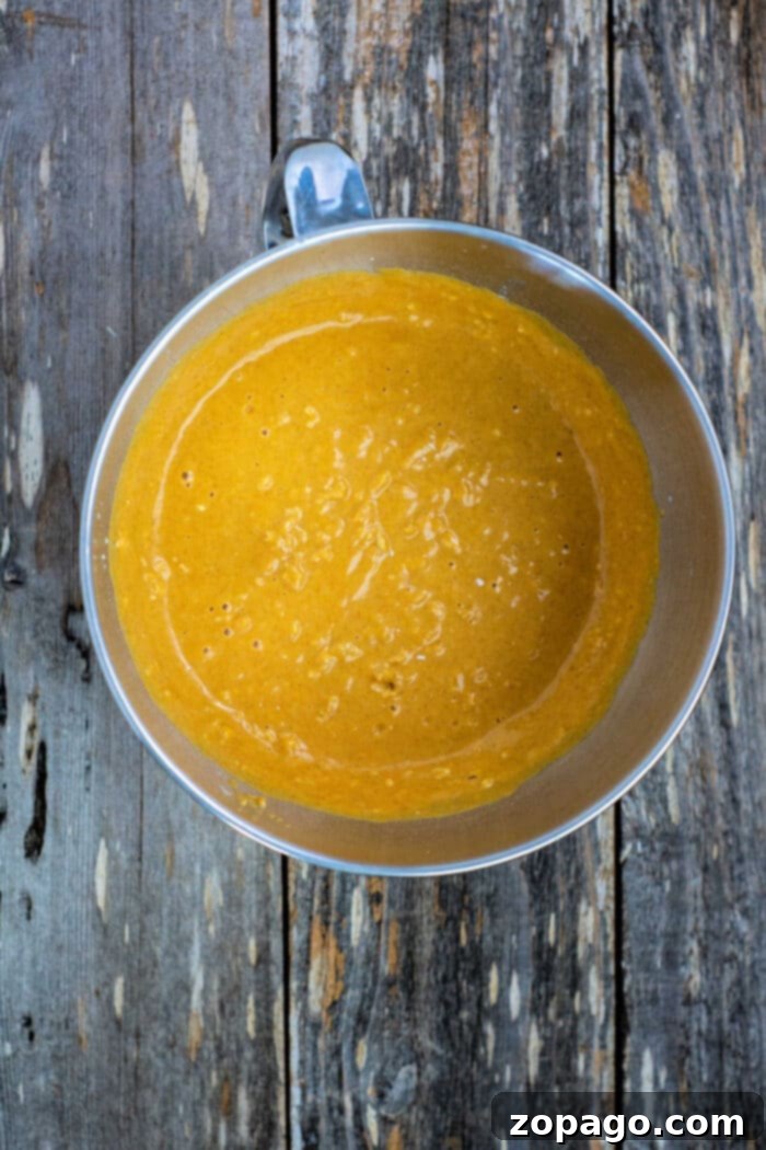 Golden Maple Pumpkin Loaf 4 A bowl of rich maple pumpkin bread batter, promising a delicious autumn treat, sits on a rustic wooden surface.