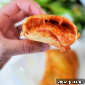 Close-up of a hand holding a half-eaten Hot Pocket, with melted cheese and sauce oozing out.