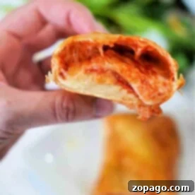 Close-up of a hand holding a half-eaten Hot Pocket, with melted cheese and sauce oozing out.