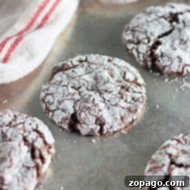 Chocolate crinkle cookies, fresh from the toaster oven, dusted with powdered sugar on a metal baking sheet near a striped cloth.