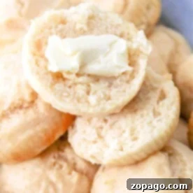 A pile of fluffy mayonnaise rolls, with one split open and topped with a dollop of butter.