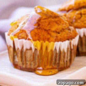 A gluten-free pumpkin muffin drizzled with honey sits on a white plate, with a blurred cloth in the background.