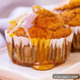 A gluten-free pumpkin muffin drizzled with honey sits on a white plate, with a blurred cloth in the background.