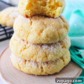 A stack of four delectable cake mix butter cookies, dusted with powdered sugar, sits on a wooden coaster. One has a playful bite taken from it, next to a vibrant green cloth.