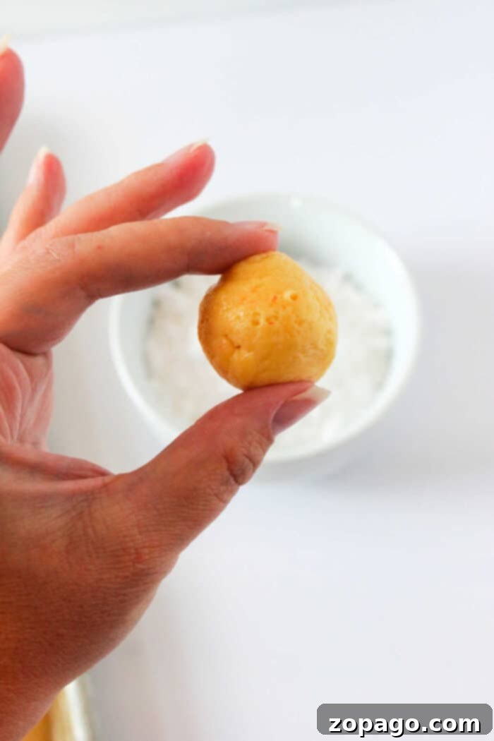 Gooey Butter Cake Mix Cookies 5 A hand delicately holds a small, round ball of cookie dough over a white bowl on a light background, evoking the satisfying allure of freshly baked cake mix butter cookies.