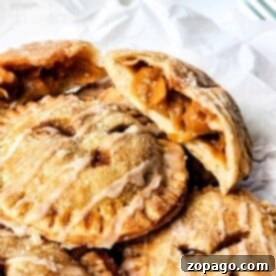 A stack of golden apple and peach hand pies, one cut open to reveal a luscious fruit filling.