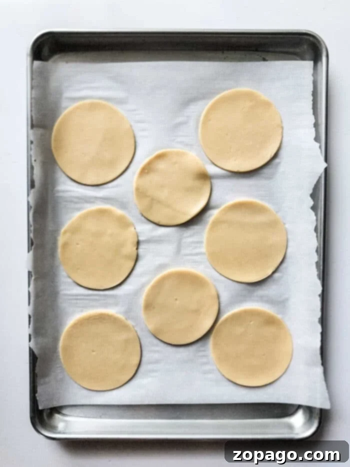 Eight round dough pieces, ready for baking, showcasing the preparation of peach hand pies on a parchment-lined baking sheet.