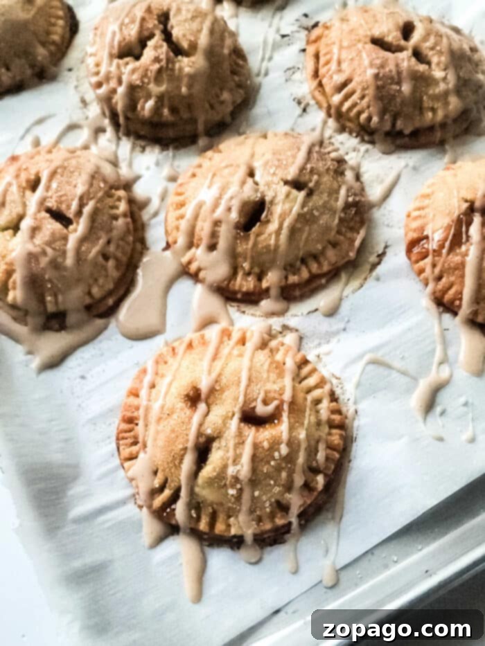 Mini peach hand pies, beautifully drizzled with icing, invitingly displayed on a baking sheet after baking.